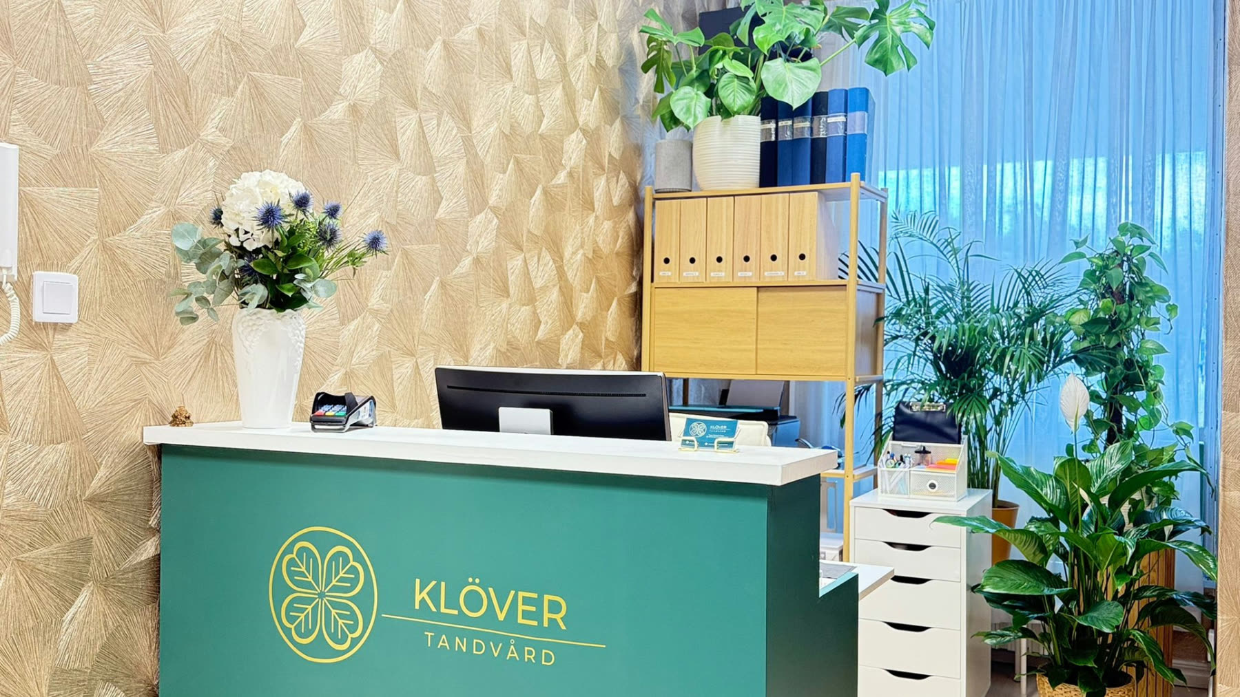 Receptionen på Klöver Tandvård i Skärholmen med klinikens gröna disk och guldfärgade klöverlogotyp på väggen